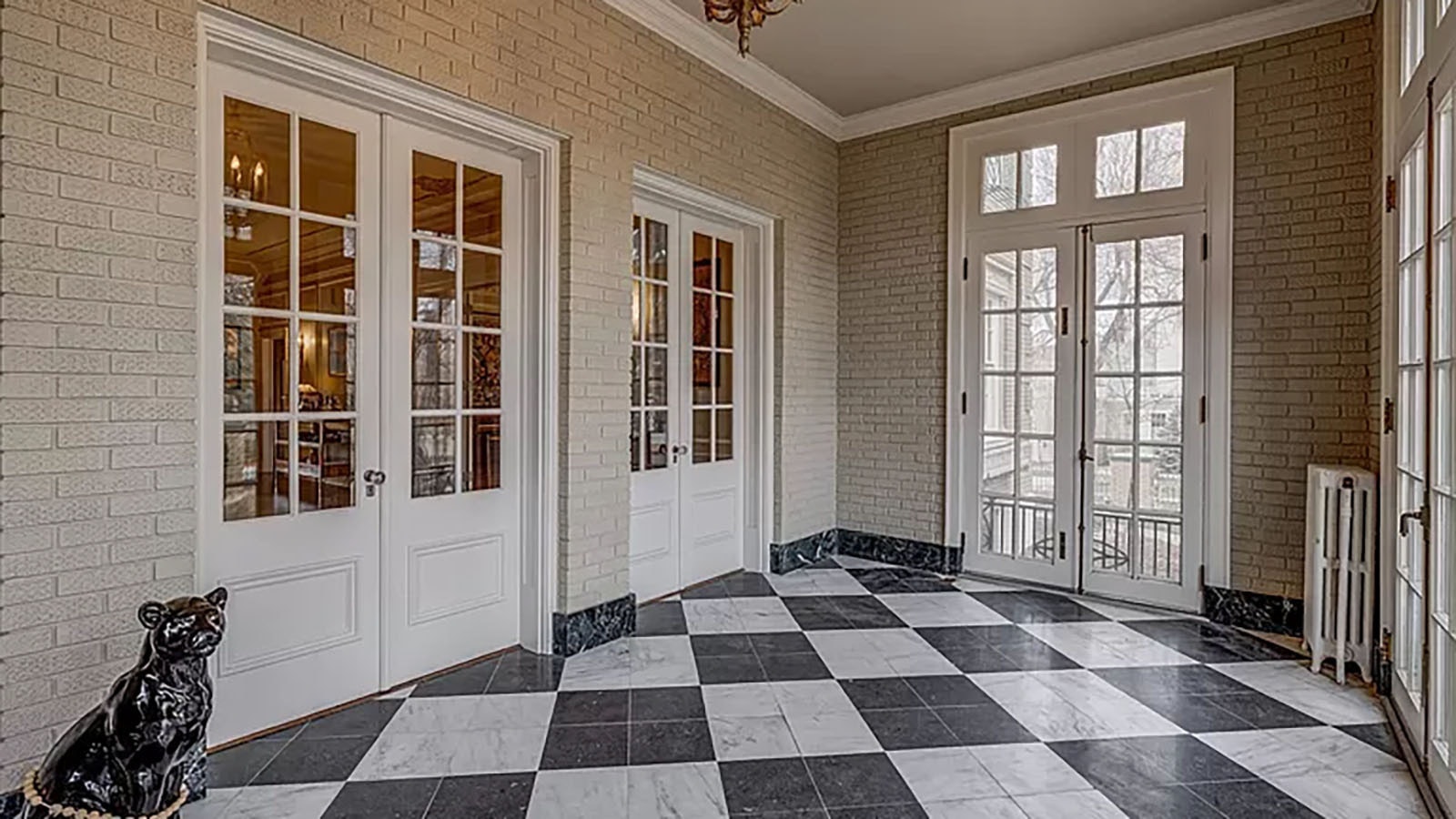 Three sets of doors lead of the greeting area of the mansion that offers checkered marble floors.