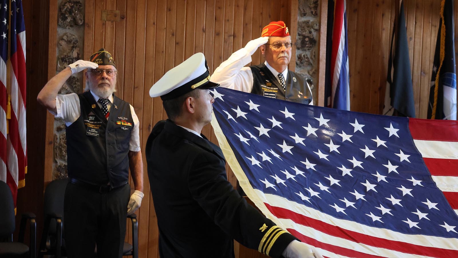 Ernie Blackford, left, and Hank Laurenz salute the unfurled flag held by Lt. Commander Tyler Shang.
