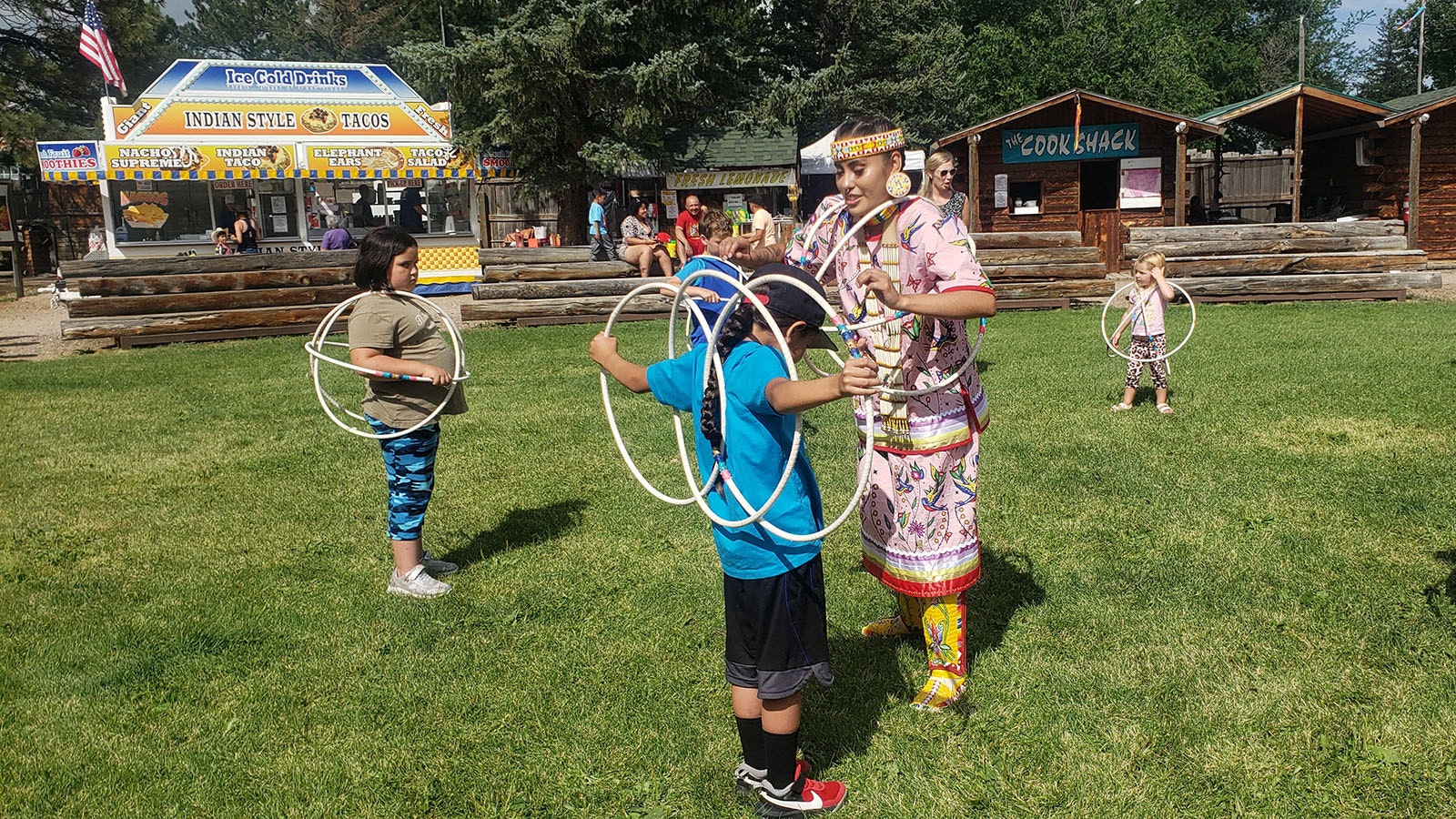 Zariah June Whiteplume assists a child with hoops to make butterfly wings in a hoop dancing workshop for children.