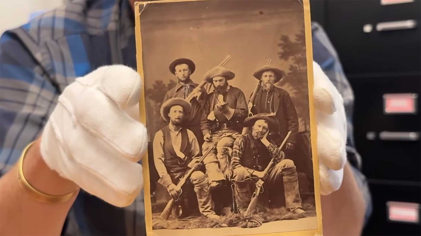 In the lower right corner, a younger Jim Baker rests his head on one hand and holds his rifle with the other. The rifle is displayed at Little Snake River Museum. The identity of the other men is not yet known.