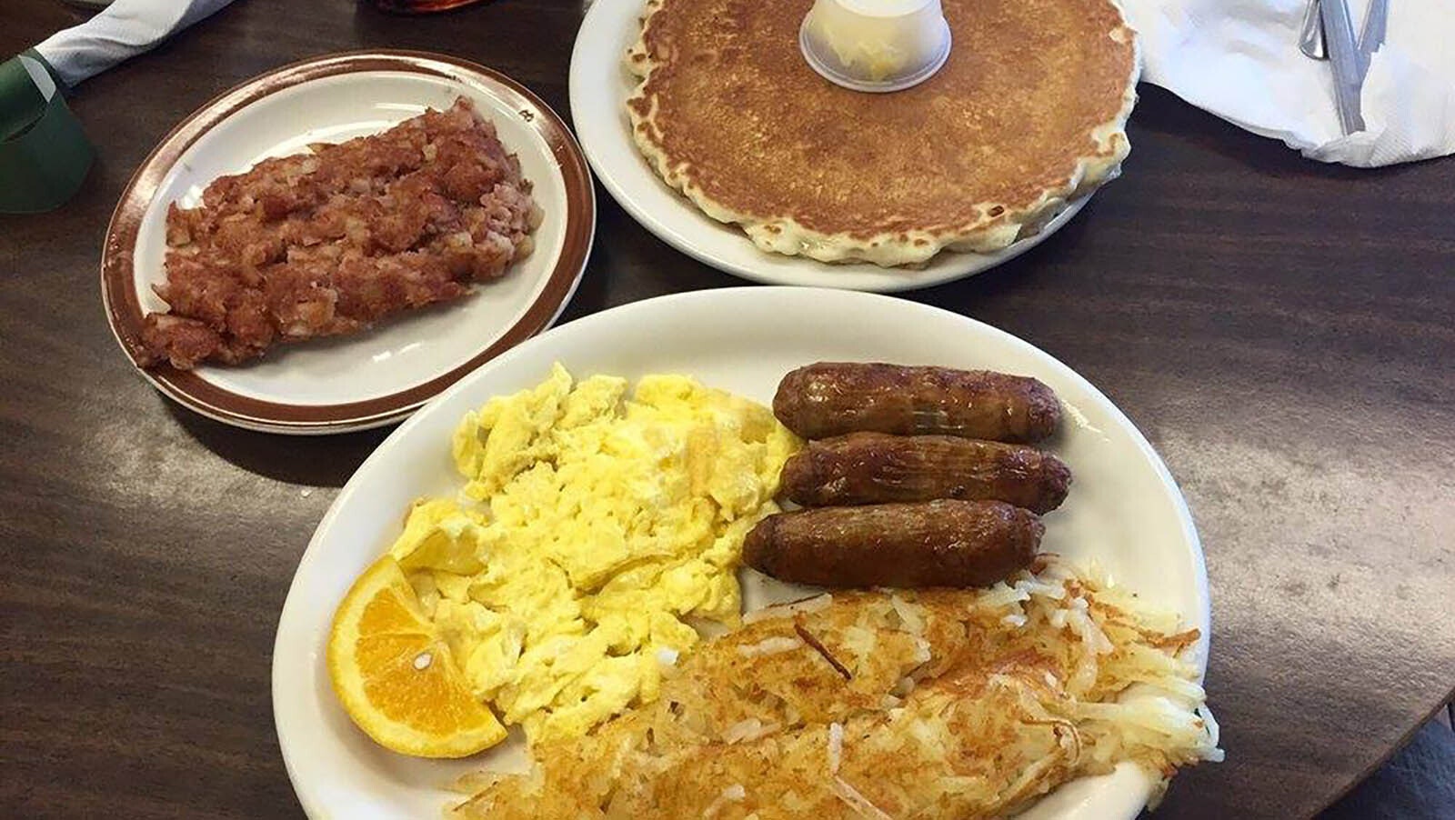 A big breakfast, with pancakes, eggs, hash browns, sausage and hash.