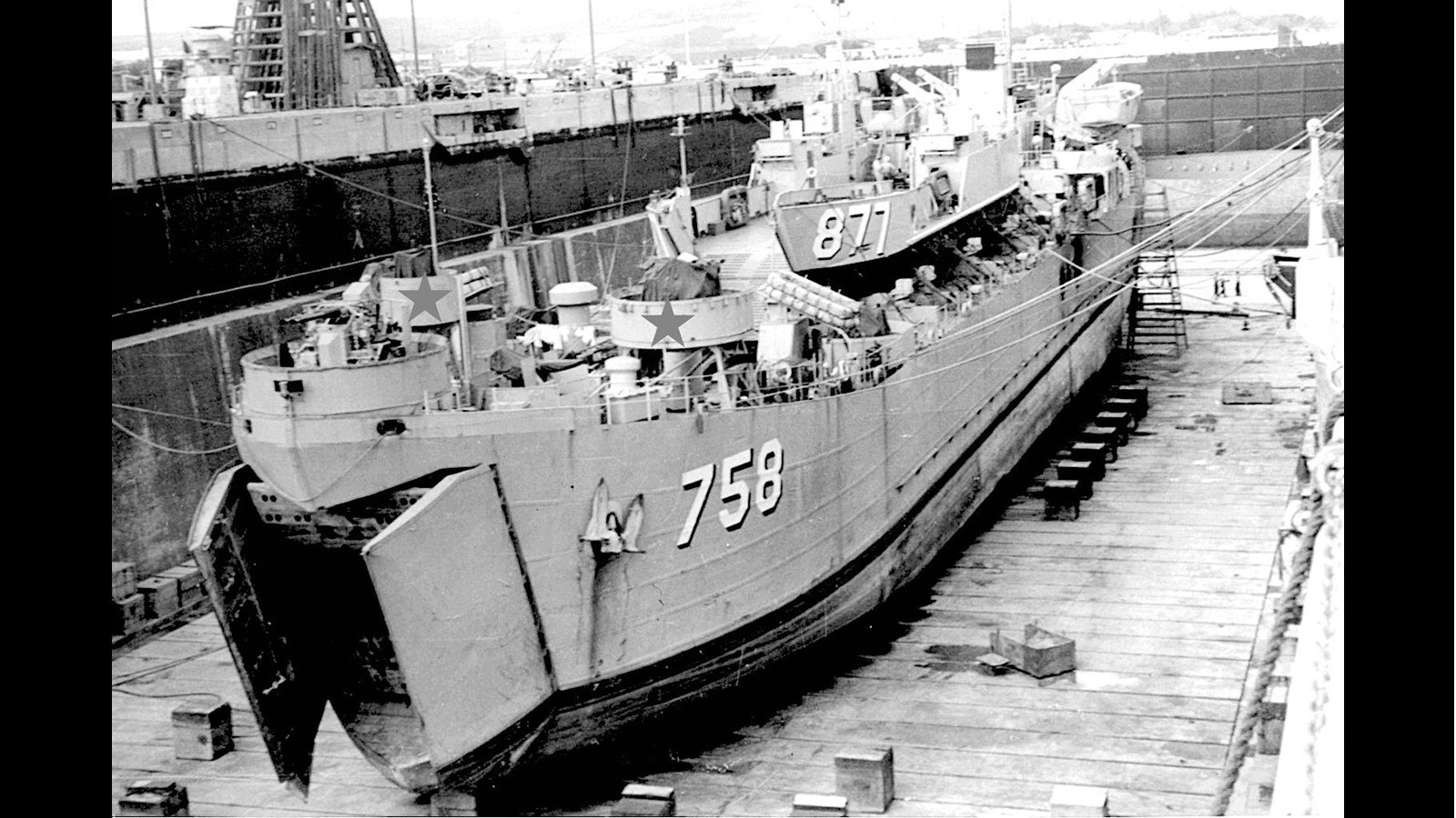 LST-758 show is in dry dock in 1960. Donald Siegel's gunner station would be one of the two platforms marked with stars located behind the twin 40 mm guns at the bow (front).