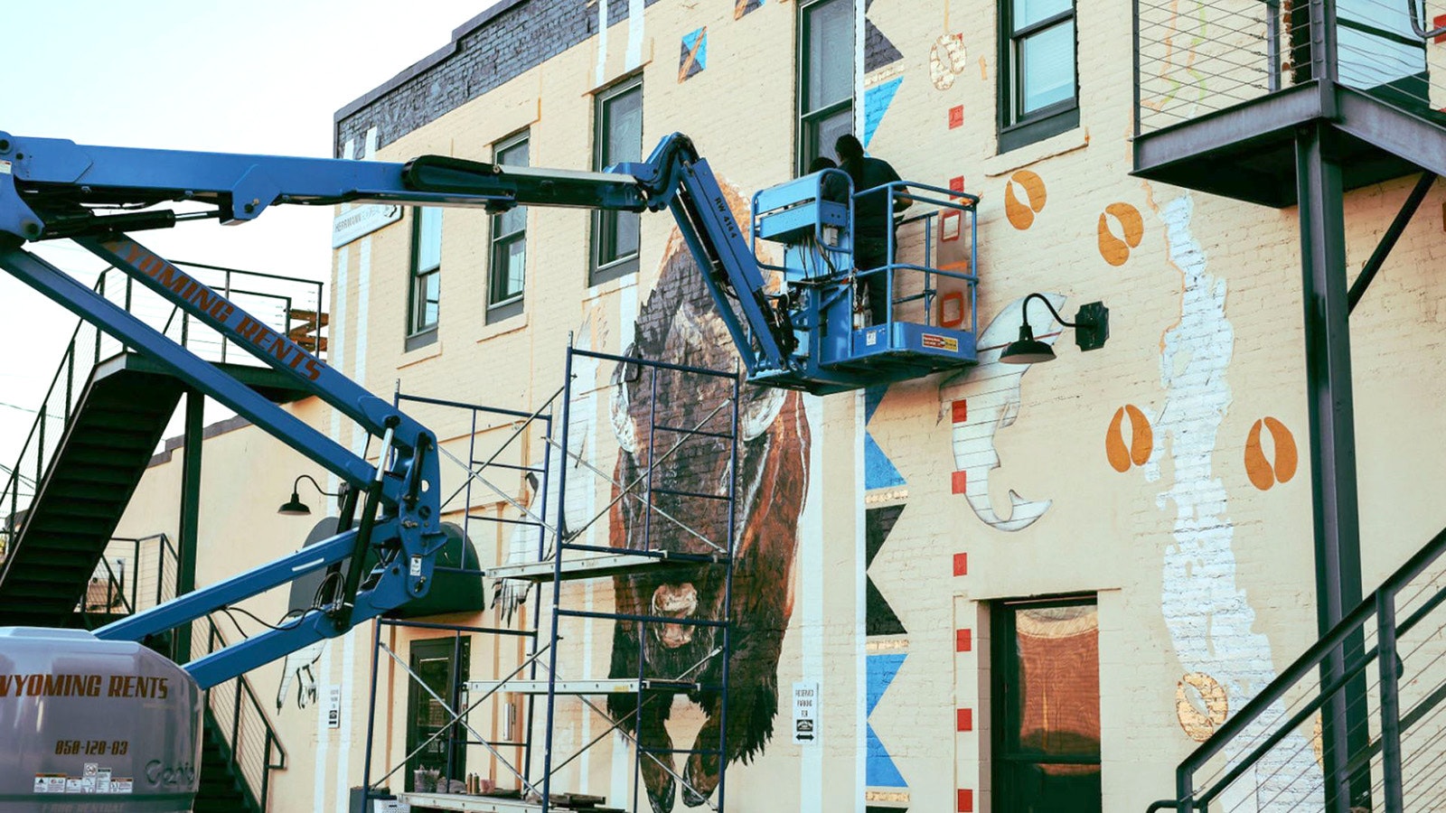 An artist works to create a large mural on a building in downtown Lander.