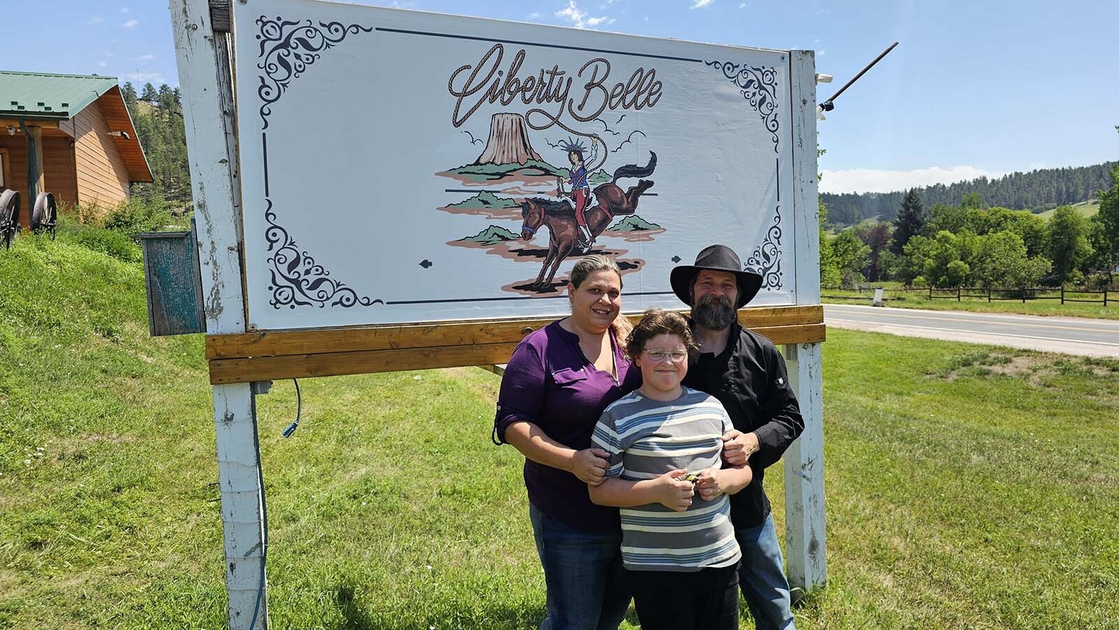 Julia Okitsu, left, with Kyle Meade and their son pose by their newly installed Liberty Belle lodge sign in Aladdin. The couple are restoring the lodge, after moving to Aladdin from the state of Washington to escape city life.