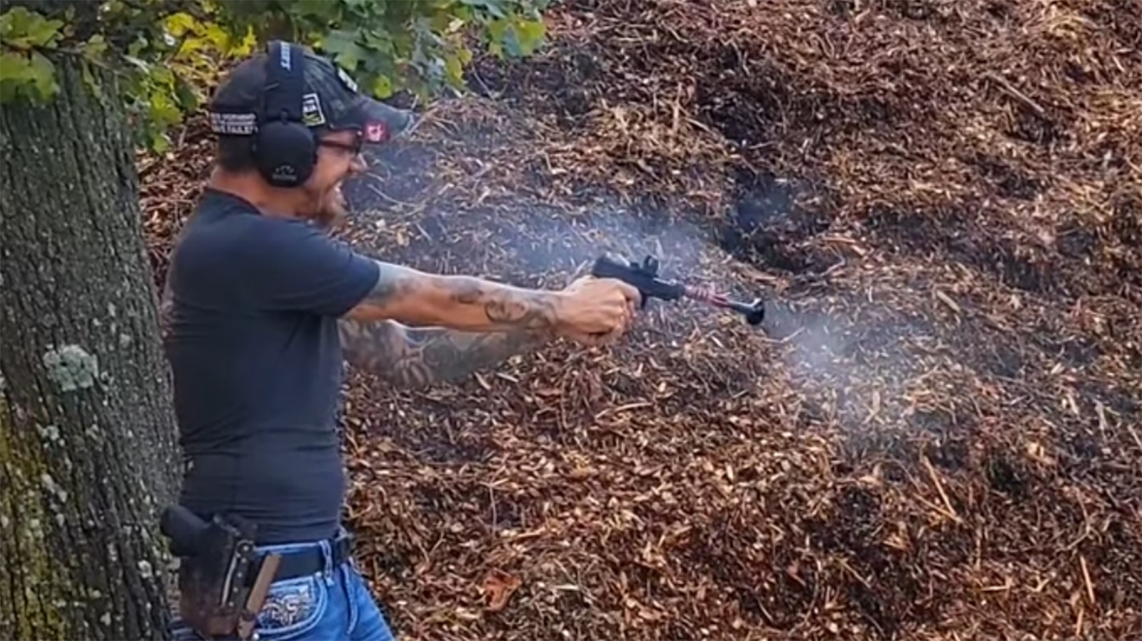 A shooter wears ear protection as he demonstrates a pistol equipped with a "loudener," in this case a funnel-like device attached to the end of the gun to amplify its sound.