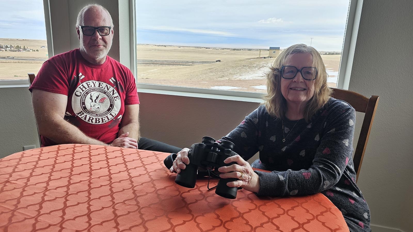 Marcy Curran with her husband Marty. Behind them, in the window, is an observatory Marty has built at their new home, outside of Cheyenne and away from overhead lights.