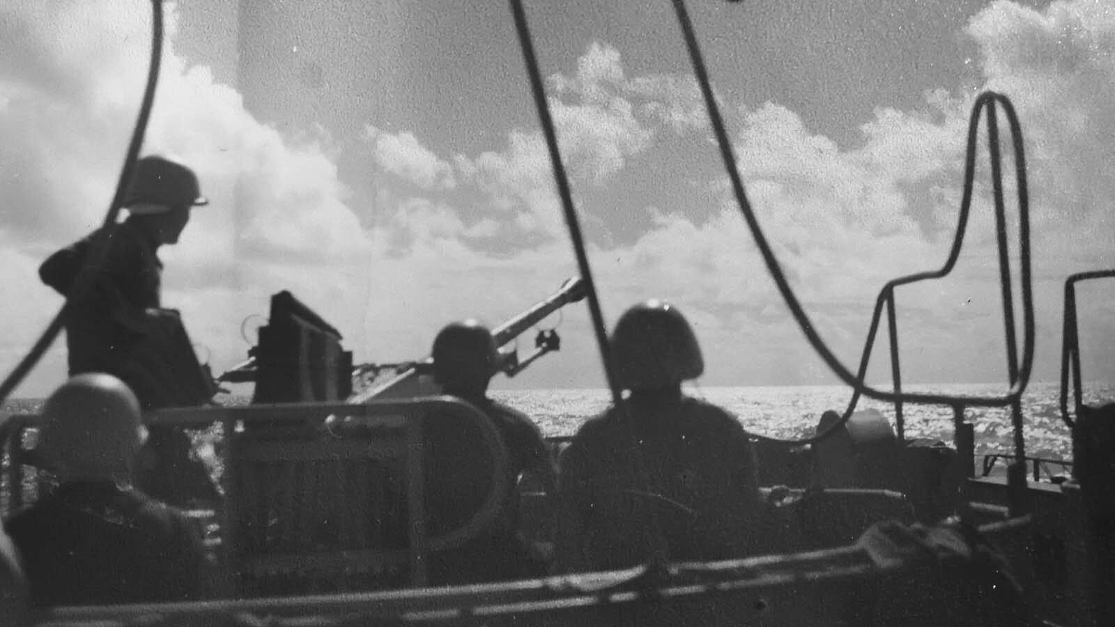 Sailors man a gun station on a ship during apparent combat action.