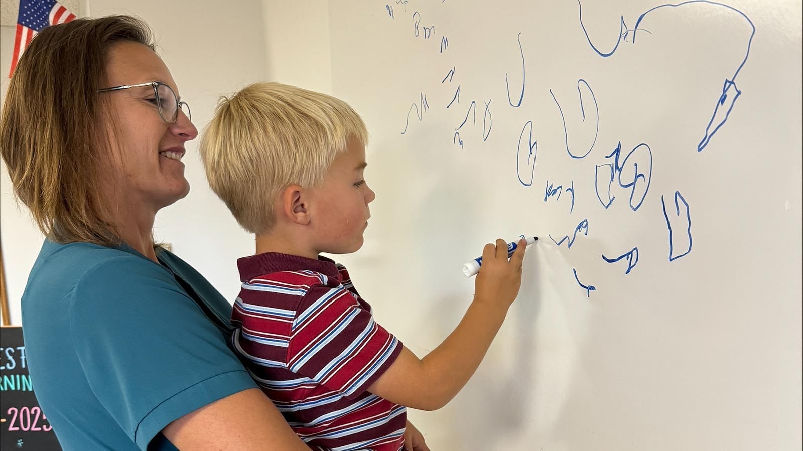 Homestead Learning co-founder, Jenna Walker, holds her 4-year-old son, Sayge, as he colors on the whiteboard in the new one-room classroom.