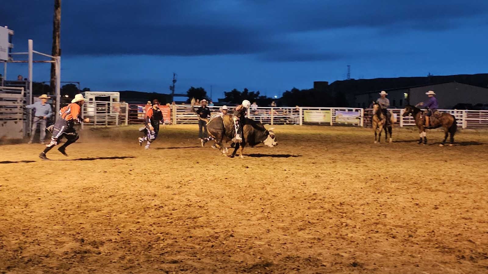 A bull and rider are off, with rodeo pickup men watching in the background, ready to move the moment they're needed.