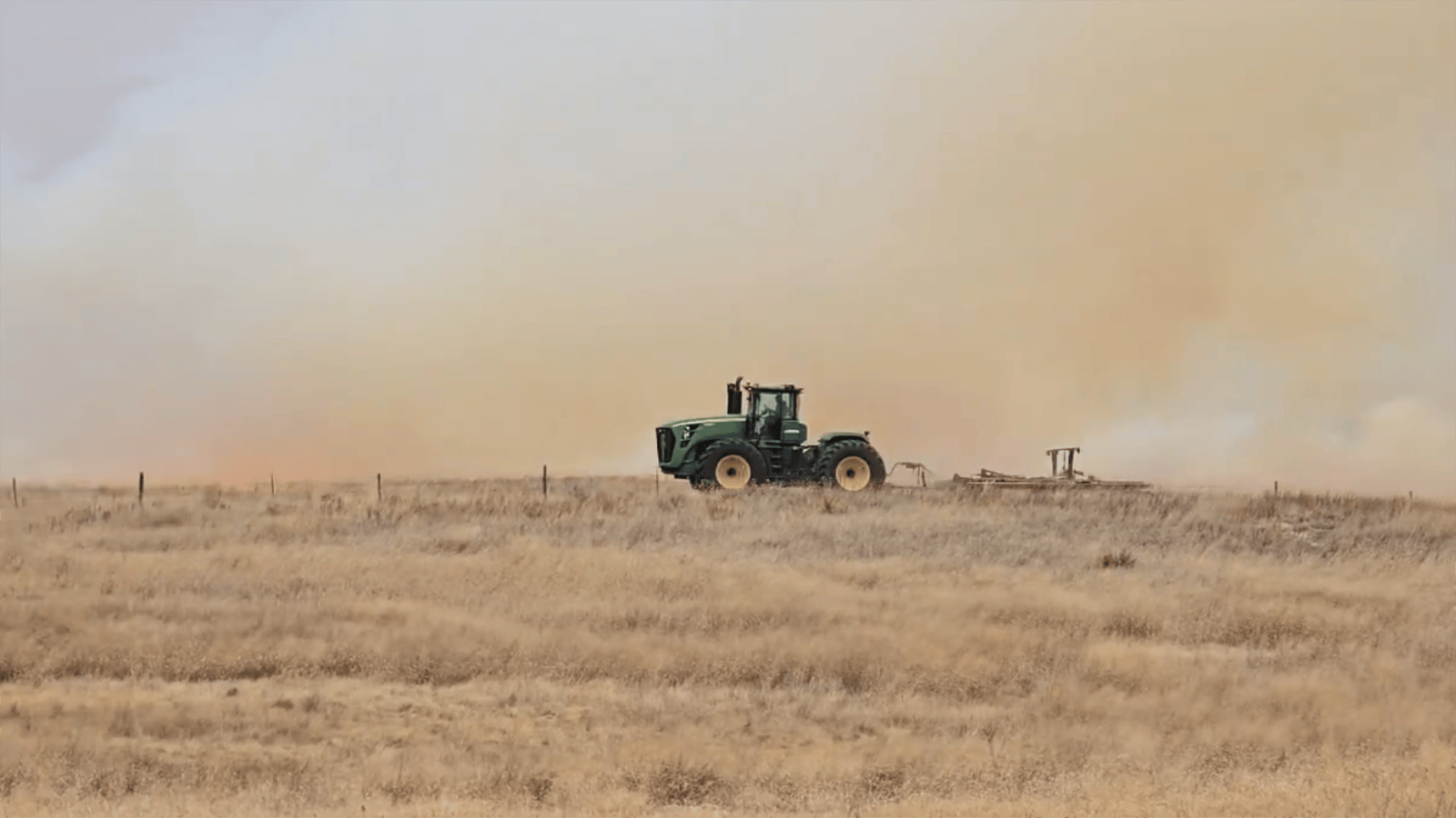 A tractor drives along a fence line as the glow of flames and thick, choking smoke billow from the Morrill Fire in Nebraska.