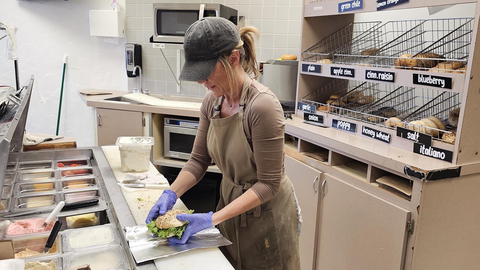 A worker named Misty prepares one of Mort's Bagels signature sandwiches using a delicious anything bagel.