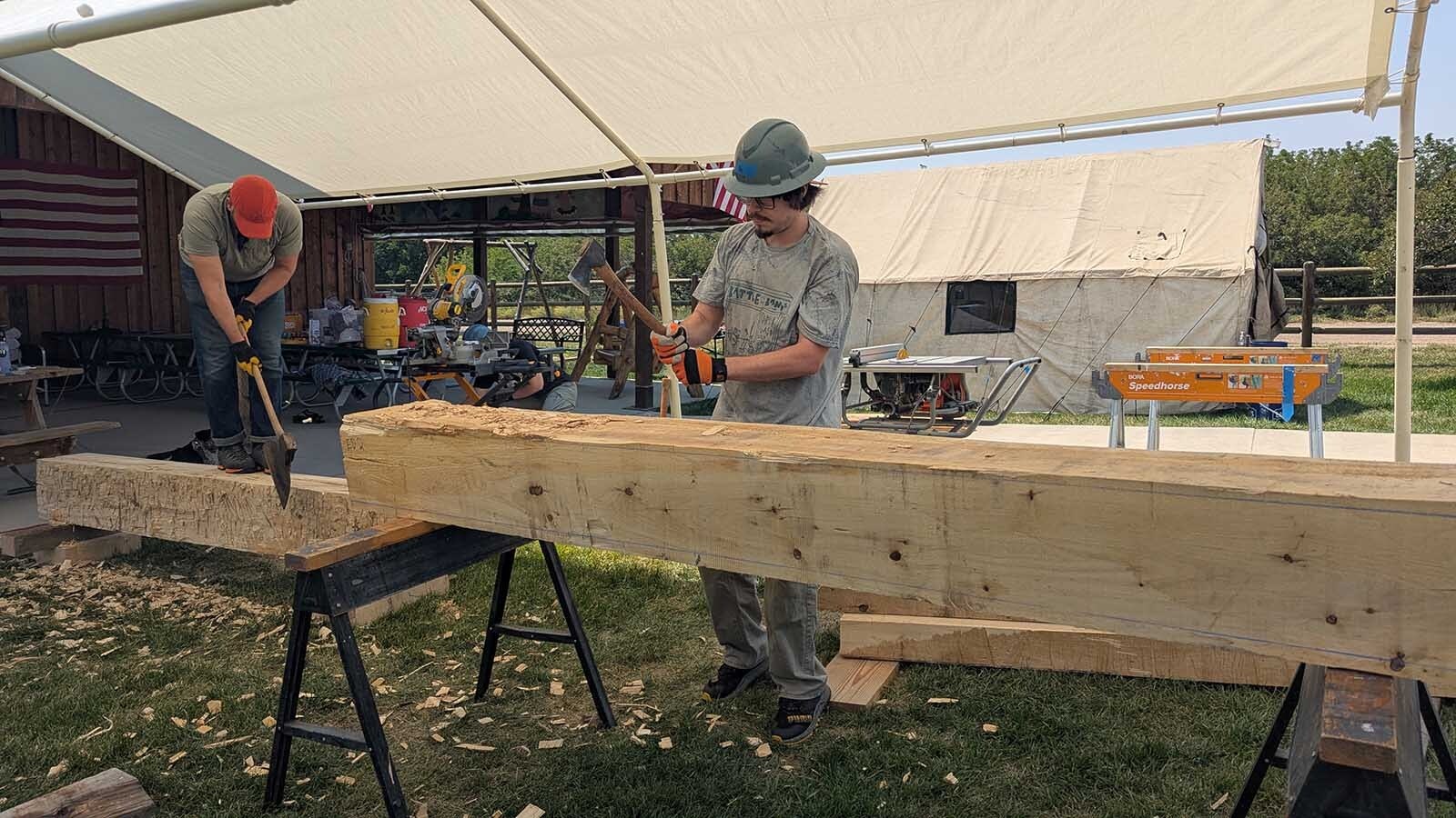 Actual broad axes are being used to shave off half an inch of wood on cottonwood logs that have been machine sawed to within an inch of the proper size.