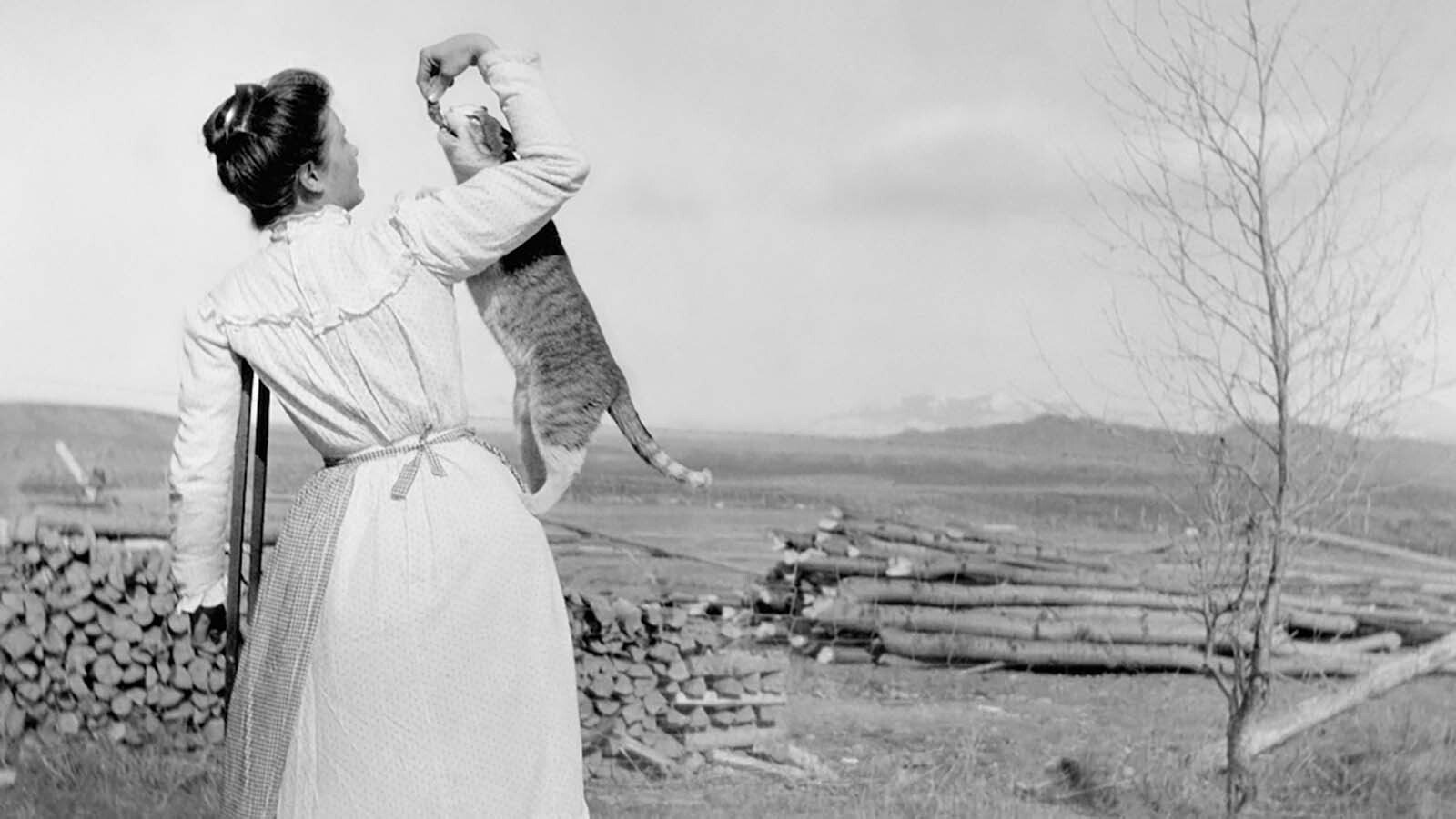 A woman feeding a pet cat with a treat in Encampment, Wyoming, in this photo by Lora Webb Nichols.