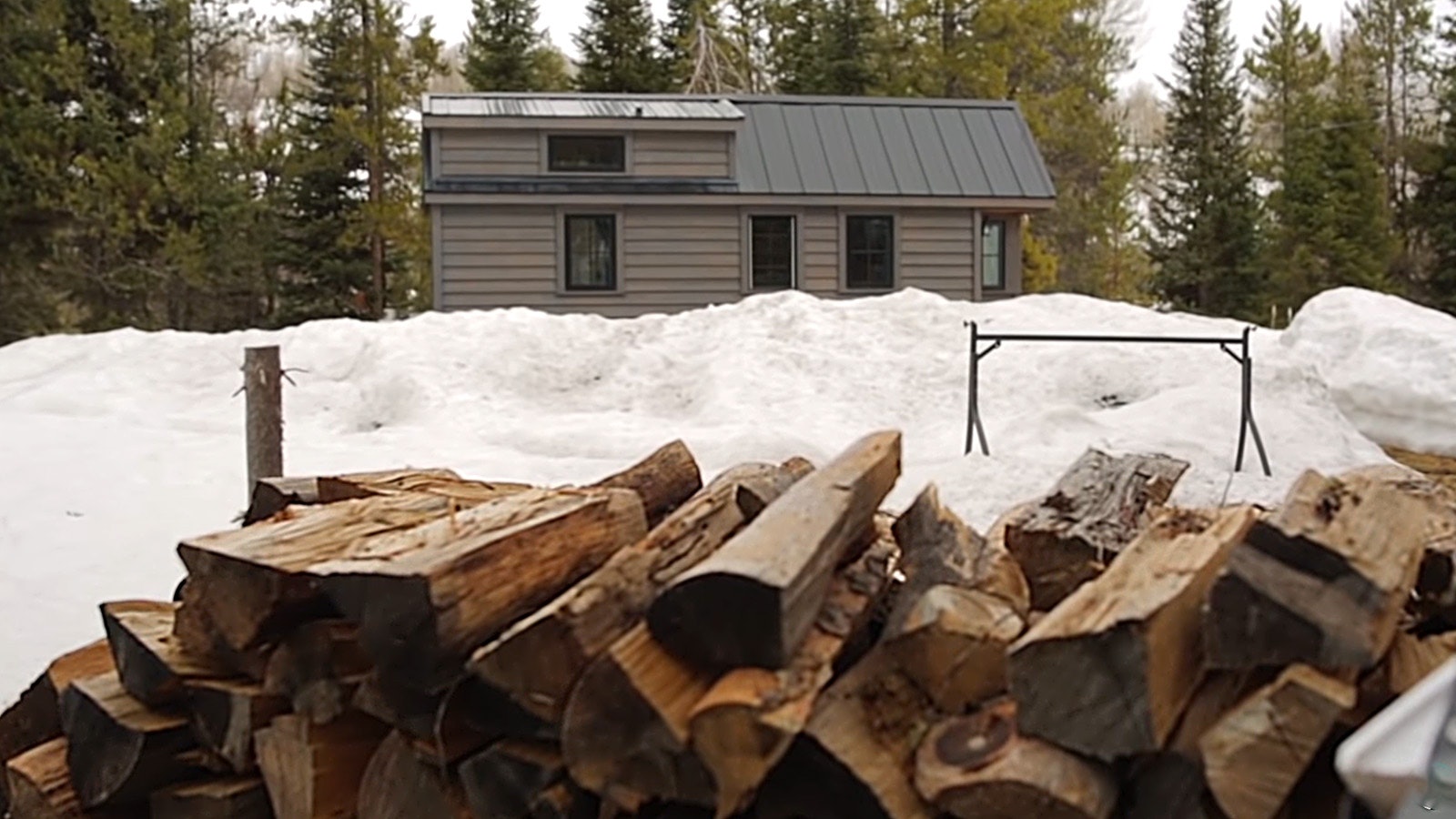A wood pile helps heat this tiny off-grid home in the northern Wyoming mountains, as featured on the Fy Nyth YouTube channel.