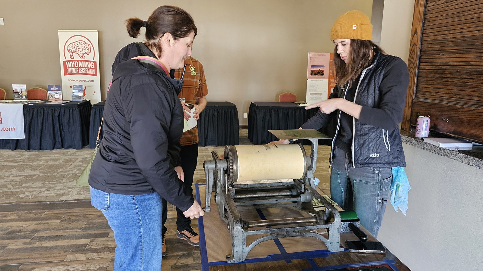 A customer slowly turns the drum left then right over an inked stencil that's been covered with a porous pice of paper, while Clark explains where the "deadbar" or deadline, is located on the printing press.