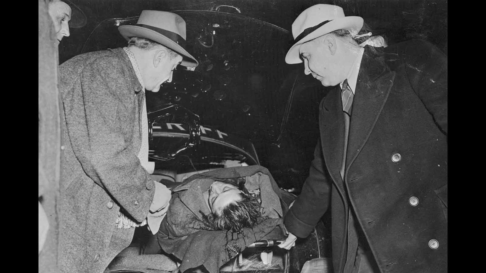 The body of Frank "The Enforcer" Nitti, is shown being removed from a squad car by two policemen, who are not identified. Nitti took his own life after a Federal Grand Jury had indicted him along with five others on charges of extorting more then two-million dollars from four large movie companies.