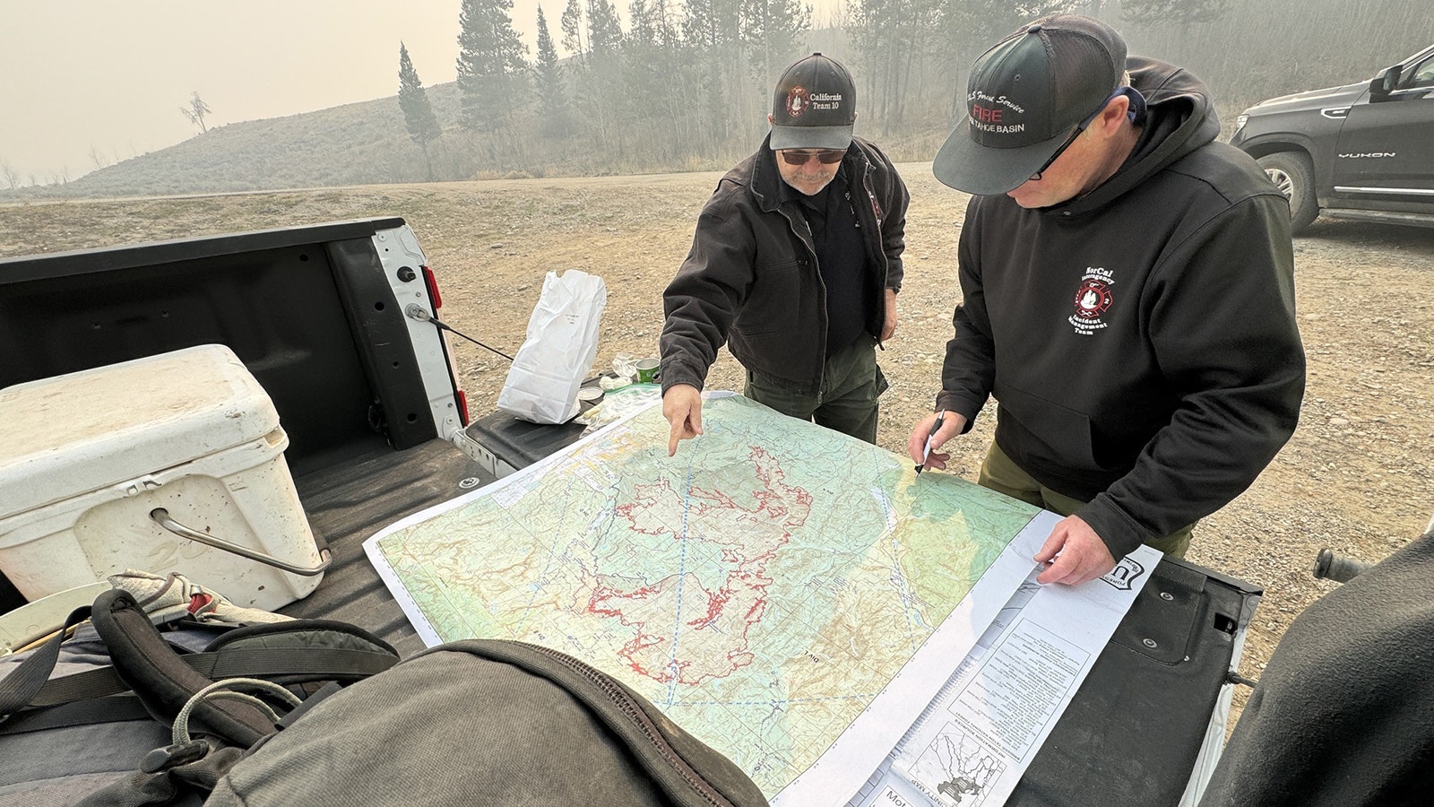 Firefighters attached to the Pack Trail Fire incident management team pore over a map of the fire, which clearly shows the Fish Creek Fire to the north and Pack Trail to the south that have merged into a single 66,000-acre fire complex.