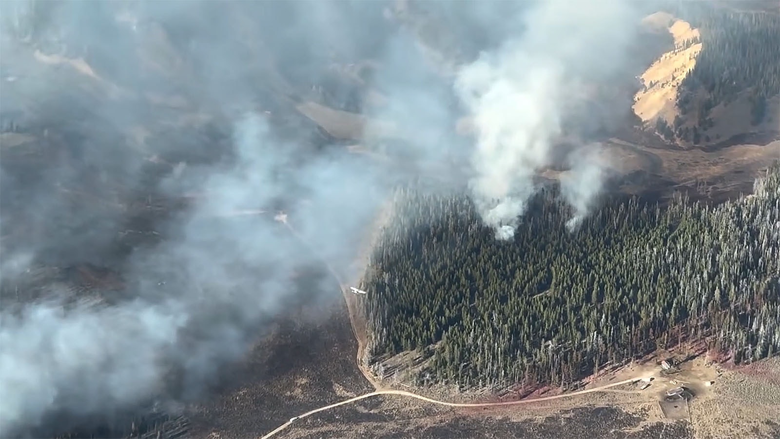 A small plane is seen from above making a run to drop retardant on spot fires burning in the Pack Trail Fire.