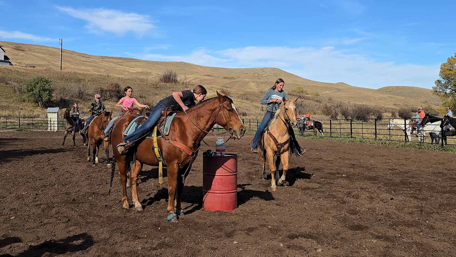 A team of riders attempts to fill a jug with water using a ladle. Eventually, one of the horses knocked the water jug over.