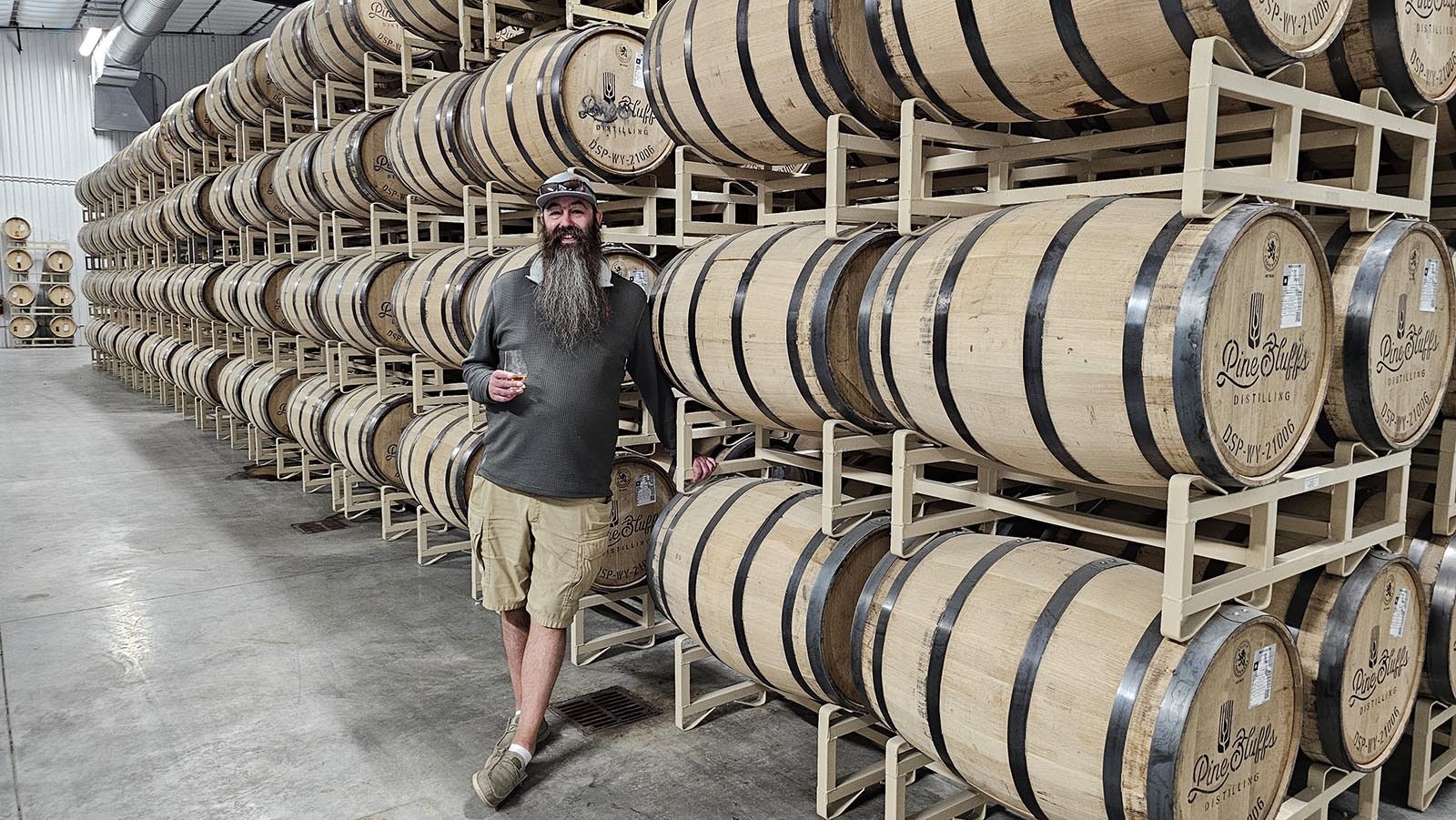 Chad Brown poses in front of a section of about 480 barrels in the backrooms of Pine Bluffs Distillery.