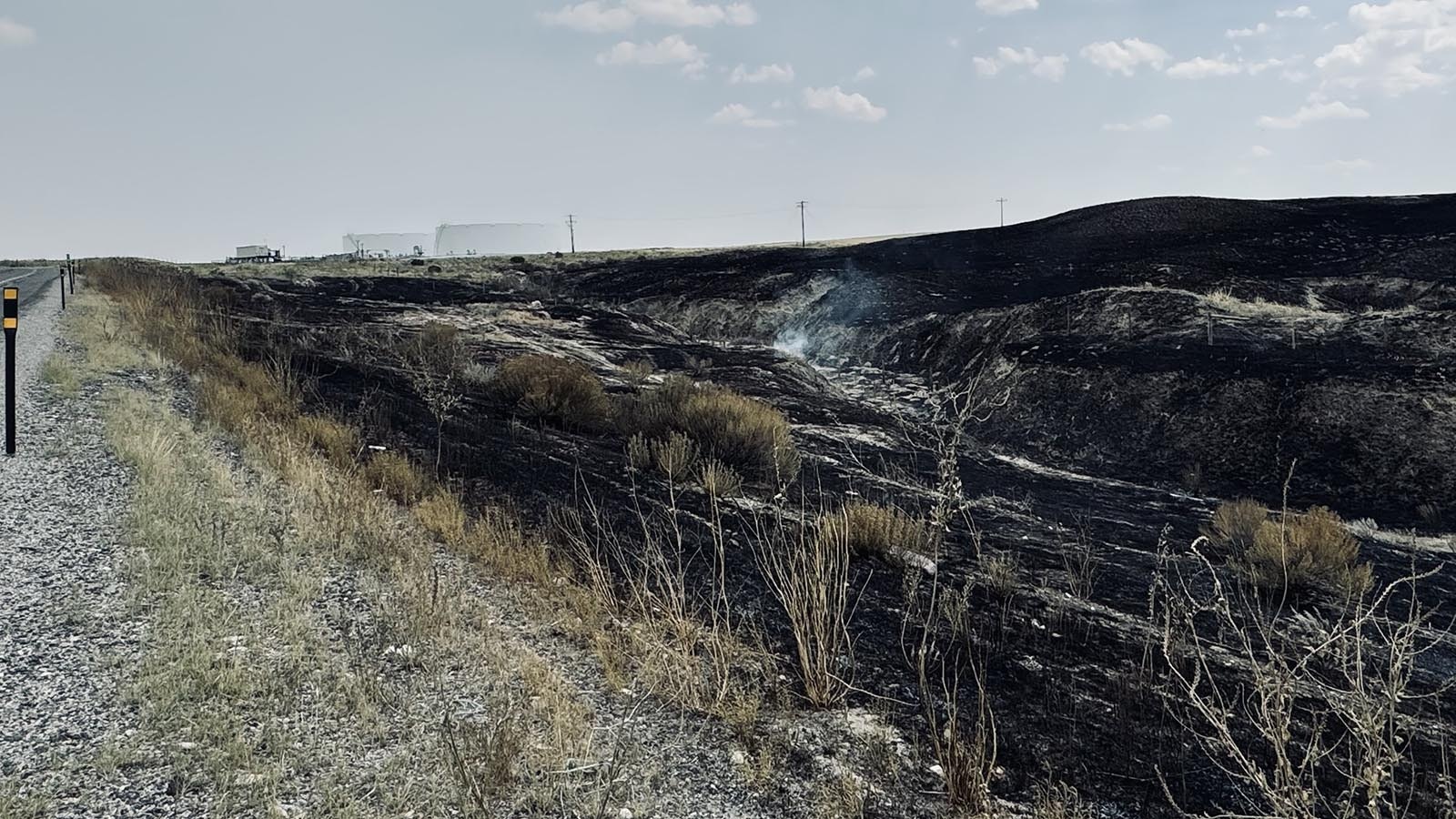 A fire smolders on Saturday south of U.S. Highway 26 near oil storage tanks owned by Tallgrass Energy in the background.