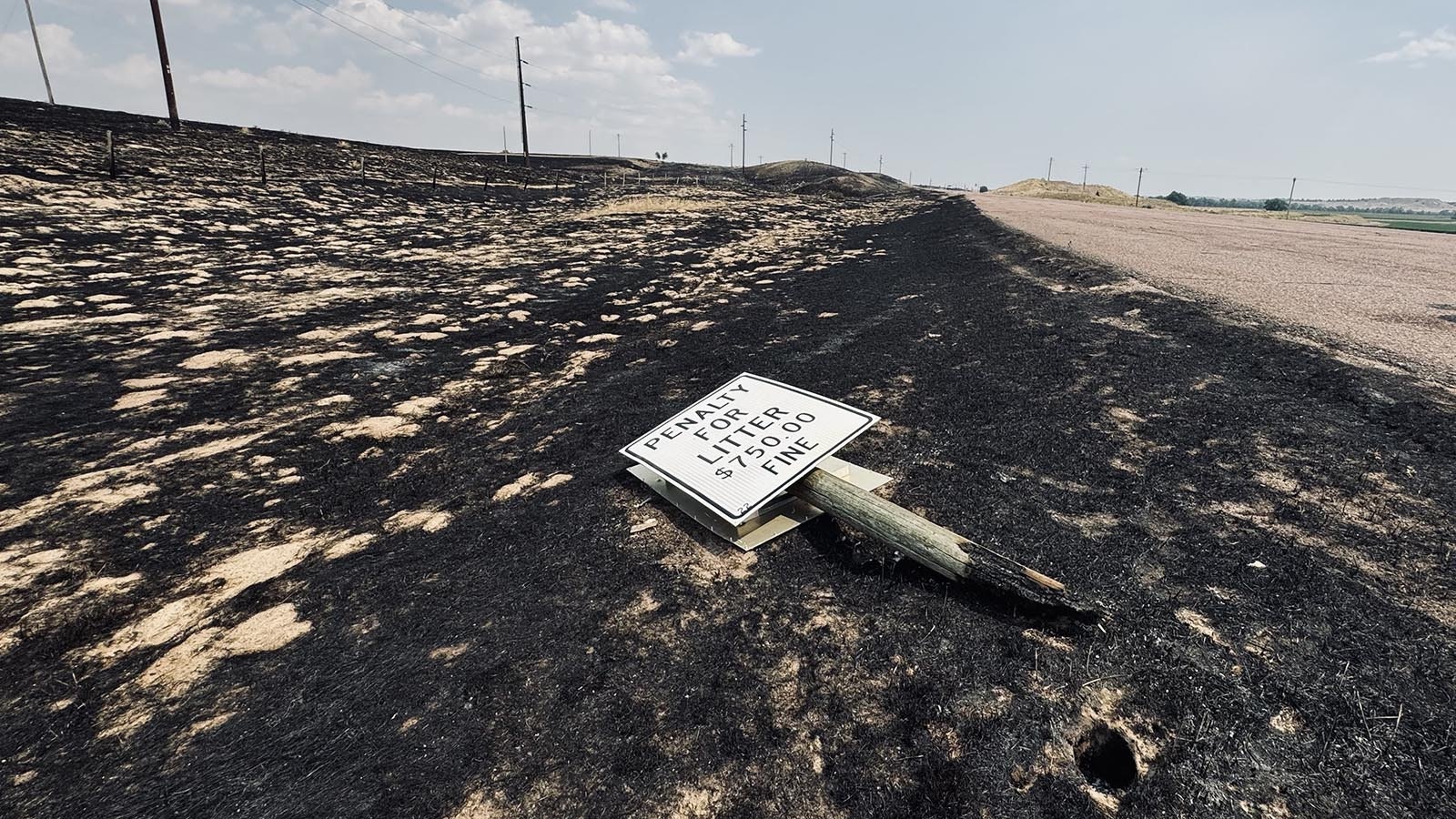 A sign fell over after burning through at its base, near a historical market for the the Cheyenne to Deadwood, South Dakota, stage trail.