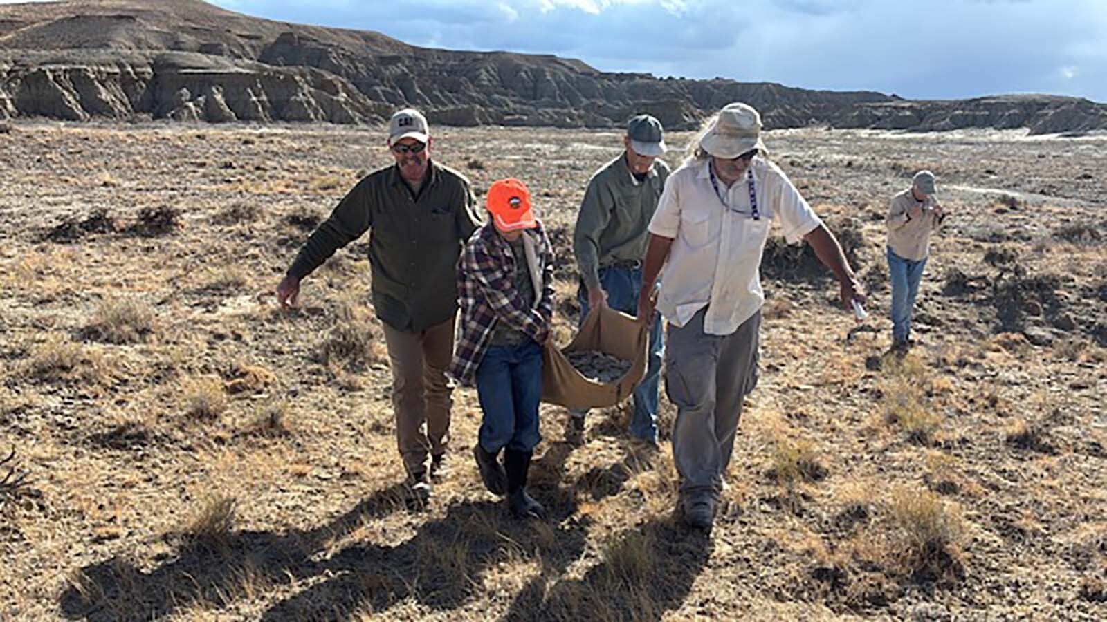 Touren Pope’s grandfather, 11-year-old Touren Pope, Tate Geological Museum volunteer Steve Felto, and museum collections specialist JP Cavigelli carry the fossilized turtle shell off BLM-managed land after excavating the specimen, as Tate Geological Museum volunteer Judith Johnston supervises.