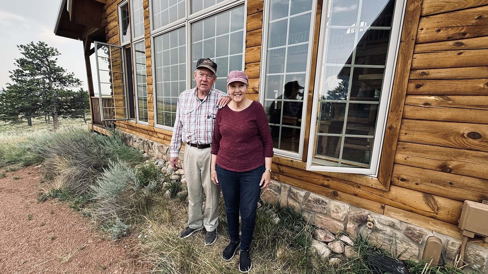 On left, John Davis and Susie Davis stand in front of an oversized picture window with panes that cover the entire northern side of their cabin overlooking the Laramie Plains. They cuddle on the couch in their living room and watch lightning storms move into the valley where a Spanish energy company wants to build a 500-megawatt wind farm.