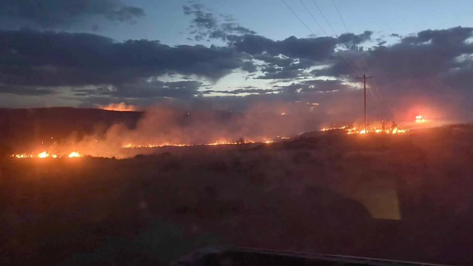 Firefighters work a glowing fireline at dusk during the Raven Creek Fire, one of two wildfires to strike the same corner of Weston County in less than a week.