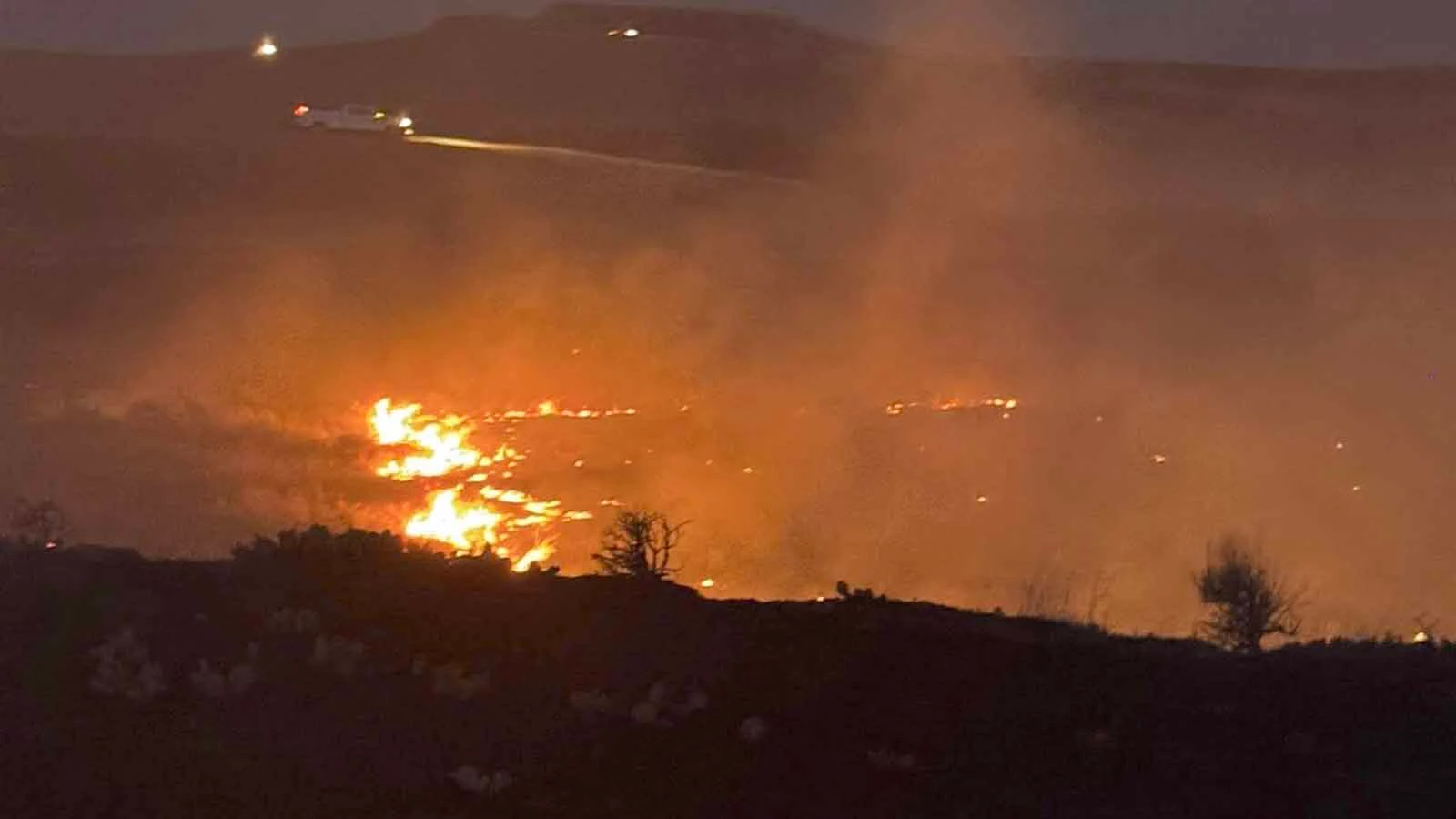 Firefighters work a glowing fireline at dusk during the Raven Creek Fire, one of two wildfires to strike the same corner of Weston County in less than a week.