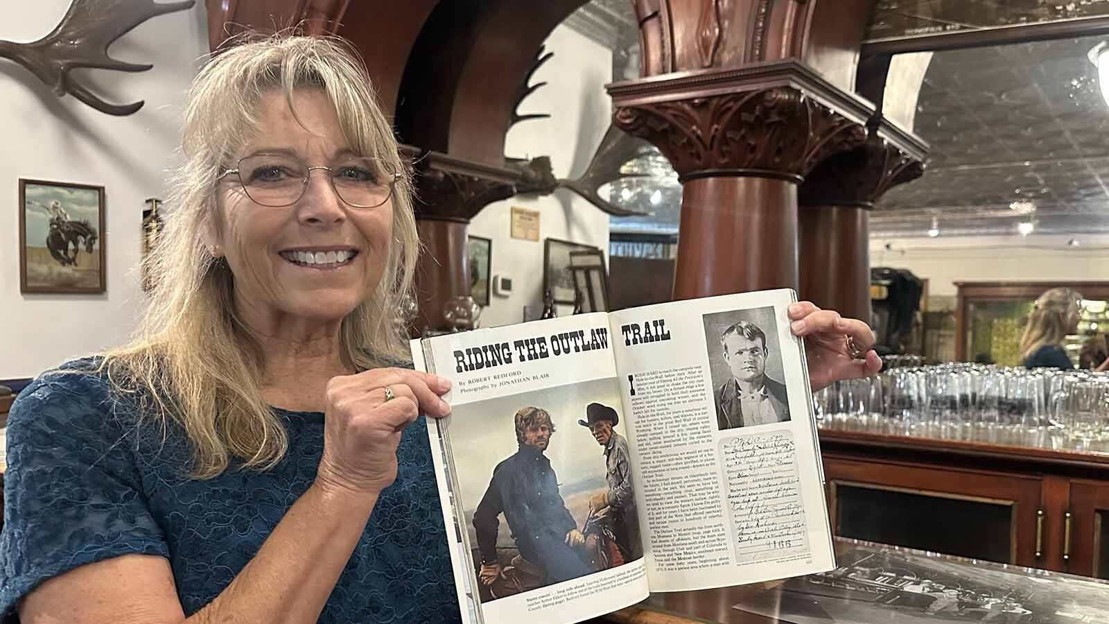 Terri Geissinger holds up the 1976 National Geographic with the cover story by Robert Redford about his outlaw ride. In 1967, he first sat at the Hole-in-the-Wall bar that now resides at the Hot Springs County Museum. The first time Redford saw the bar, it was still being used in the Hole-in-the-Wall Bar, a saloon that had first opened in the 1890s and welcomed the local outlaws in.