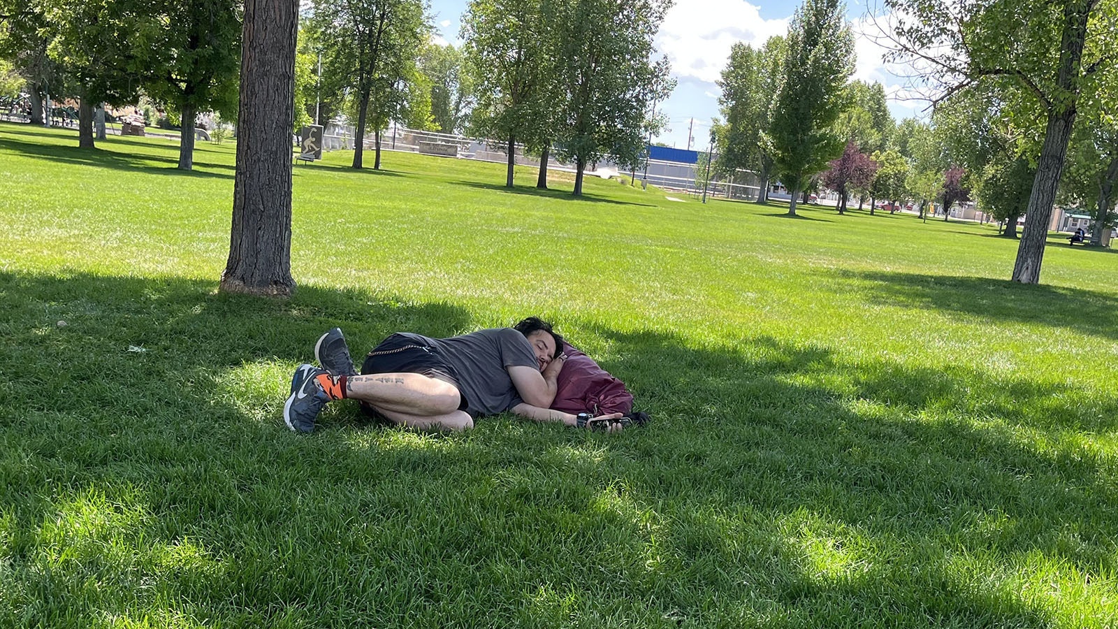 A man sleeps Tuesday in Riverton’s City Park as other wandering groups drank alcohol, joked, and asked occasional passers-by for money.
