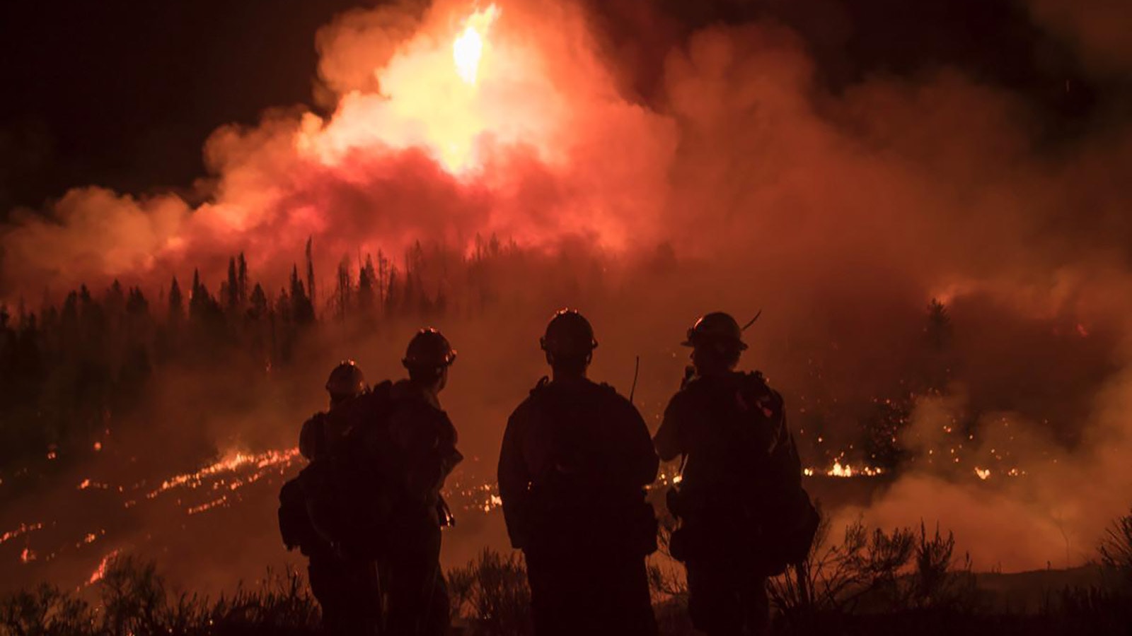A group of firefighters watch as the Roosevelt Fire burns in Wyoming in 2018.