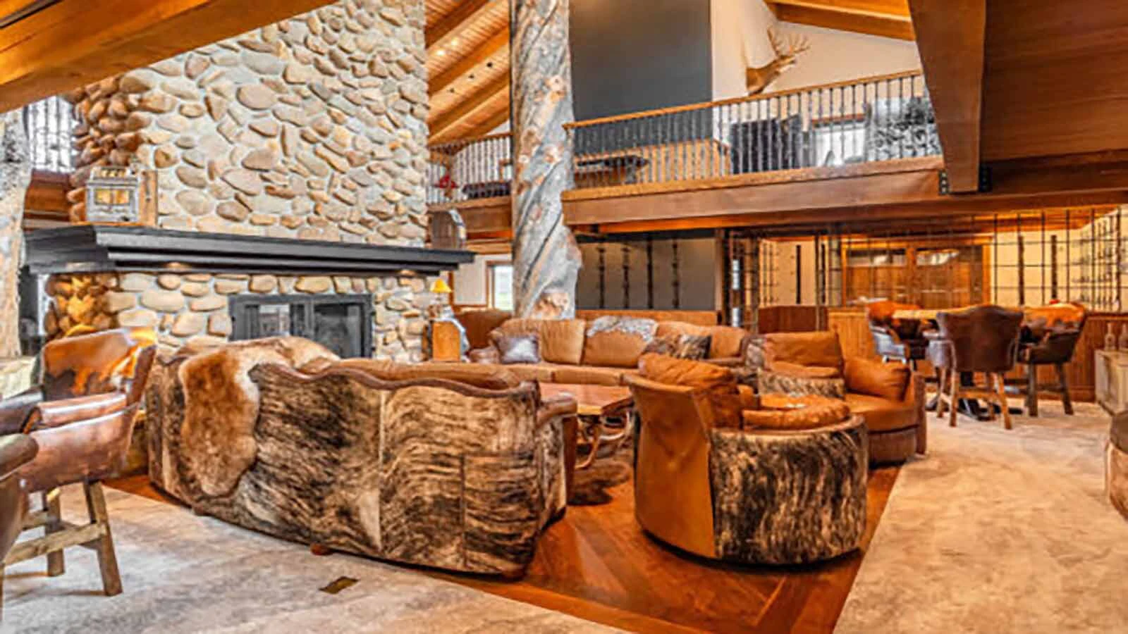 The biggest gathering space is the grand hall, where soaring ceilings, massive timber supports, and a floor-to-ceiling stone fireplace frame an entertainment area that includes a custom wet bar. Upper-level walkways overlook the room.