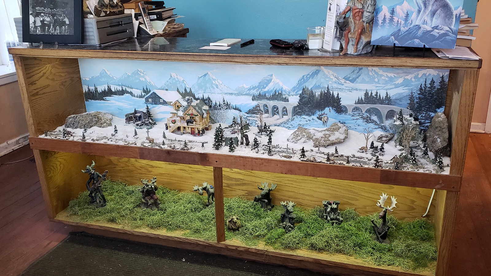The front counter includes a picture of Tracy Carotta's parents' old bar top, left, as well as dioramas that show a snowy scene with several miniature scroungy moose figurines. Below that are moose statues in goofy poses.