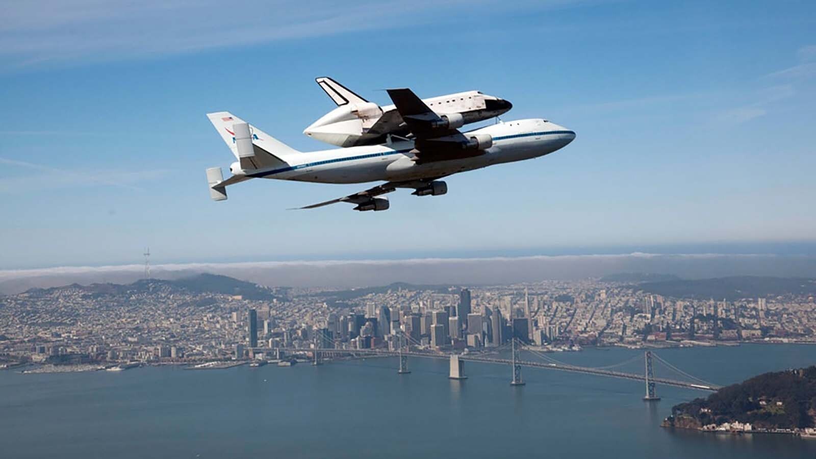 A space shuttle is flown on a 747 jet over the Golden Gate Bridge.