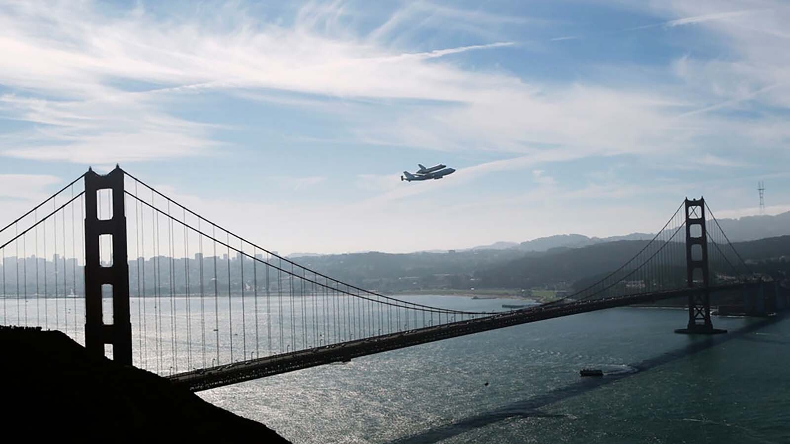 A space shuttle is flown on a 747 jet over the Golden Gate Bridge.