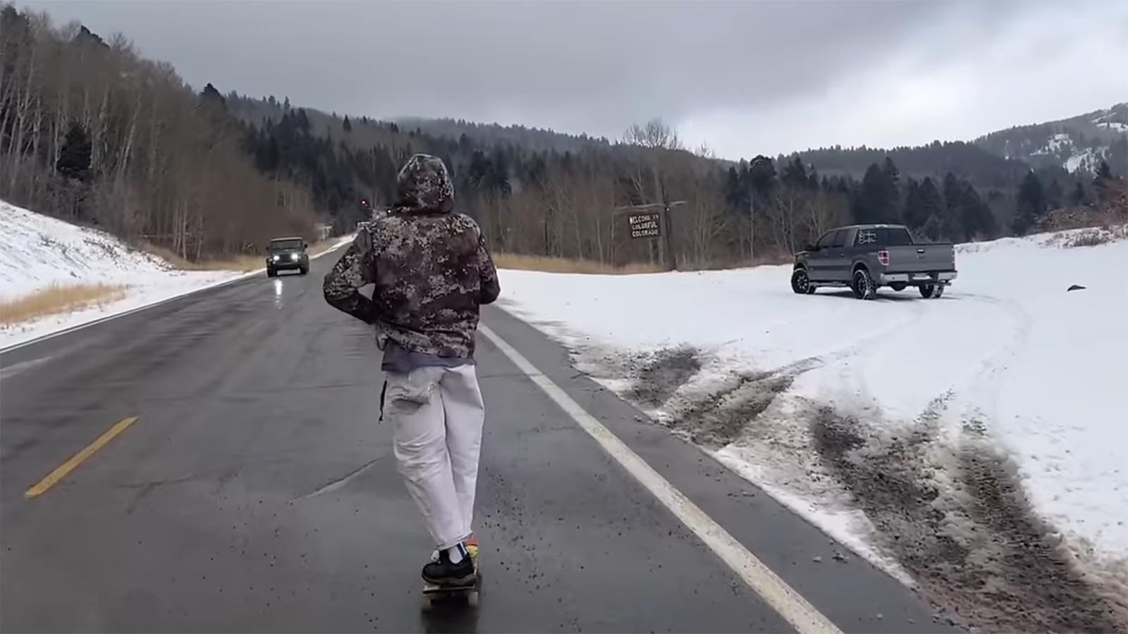 Orio Ramirez, followed by Jason Vanporppal, skateboards over a snowy Colorado mountain pass.