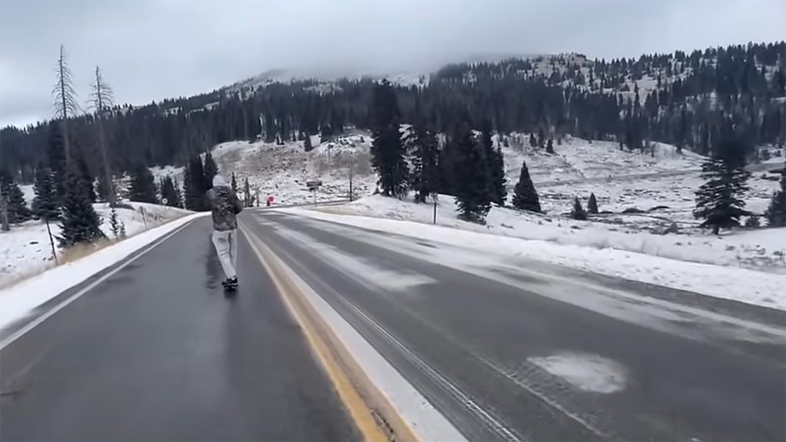 Orio Ramirez, followed by Jason Vanporppal, skateboards over a snowy Colorado mountain pass.