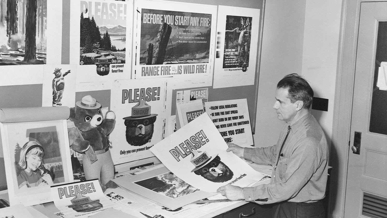 A park ranger in an office with a plethora of posters about preventing forest fires, most of which feature Smokey Bear.