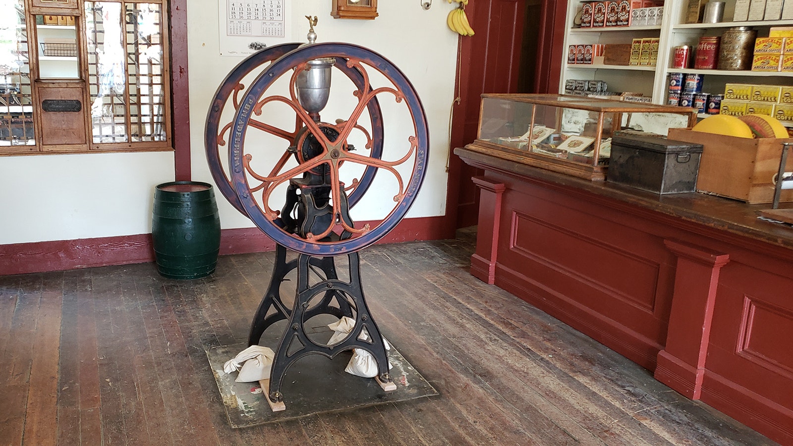 An old-fashioned coffee mill stands in the mercantile. Beans were put into the silver canister at the top and the wheel turned. Ground beans would drain out the bottom into a small box.