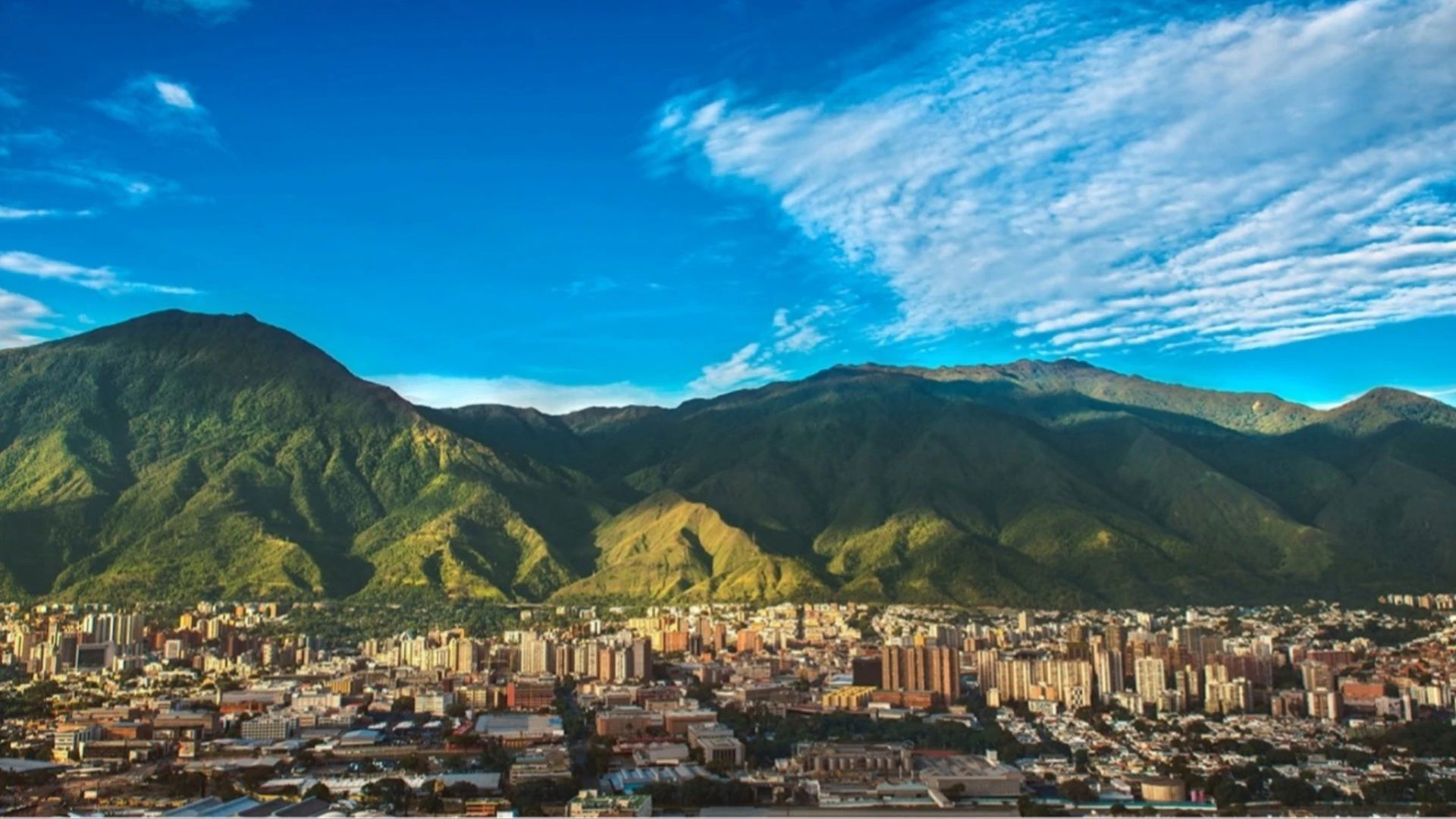 Image of the sky, green mountains and a city below. Caracas: the capital city of Venezuela.