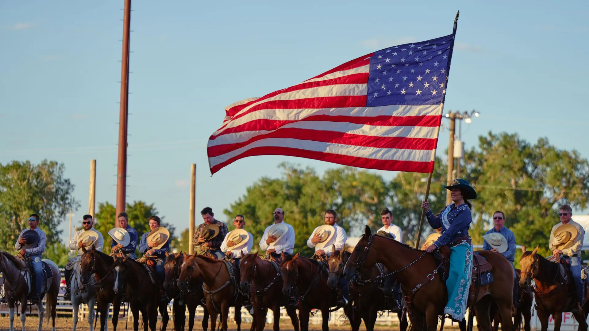 Line of people on horses with cowboy hats on their hearts and a women holding an American Flag