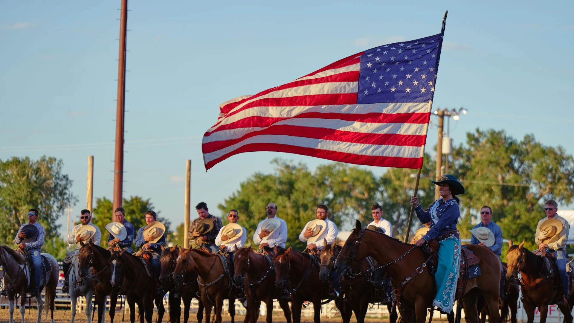 Line of people on horses with cowboy hats on their hearts and a women holding an American Flag