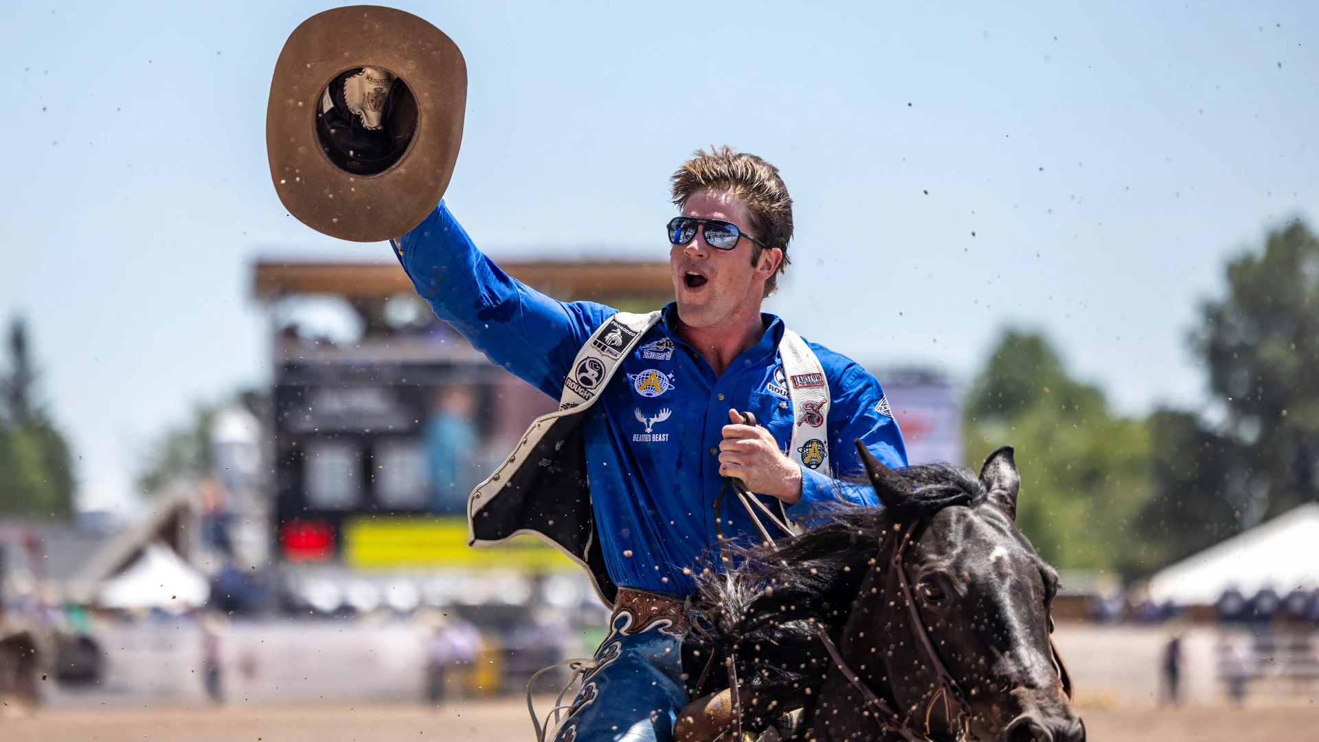 A man waving his cowboy hat and riding a horse