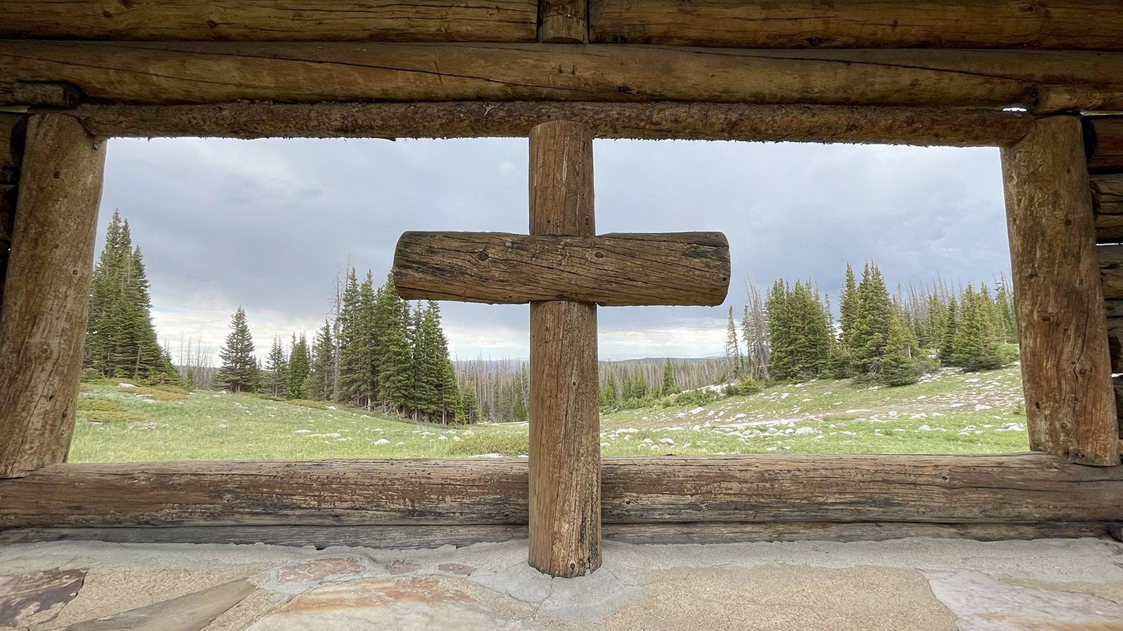 The chapel’s log walls shelter a simple, hand-hewn lodge pole cross within the open window.