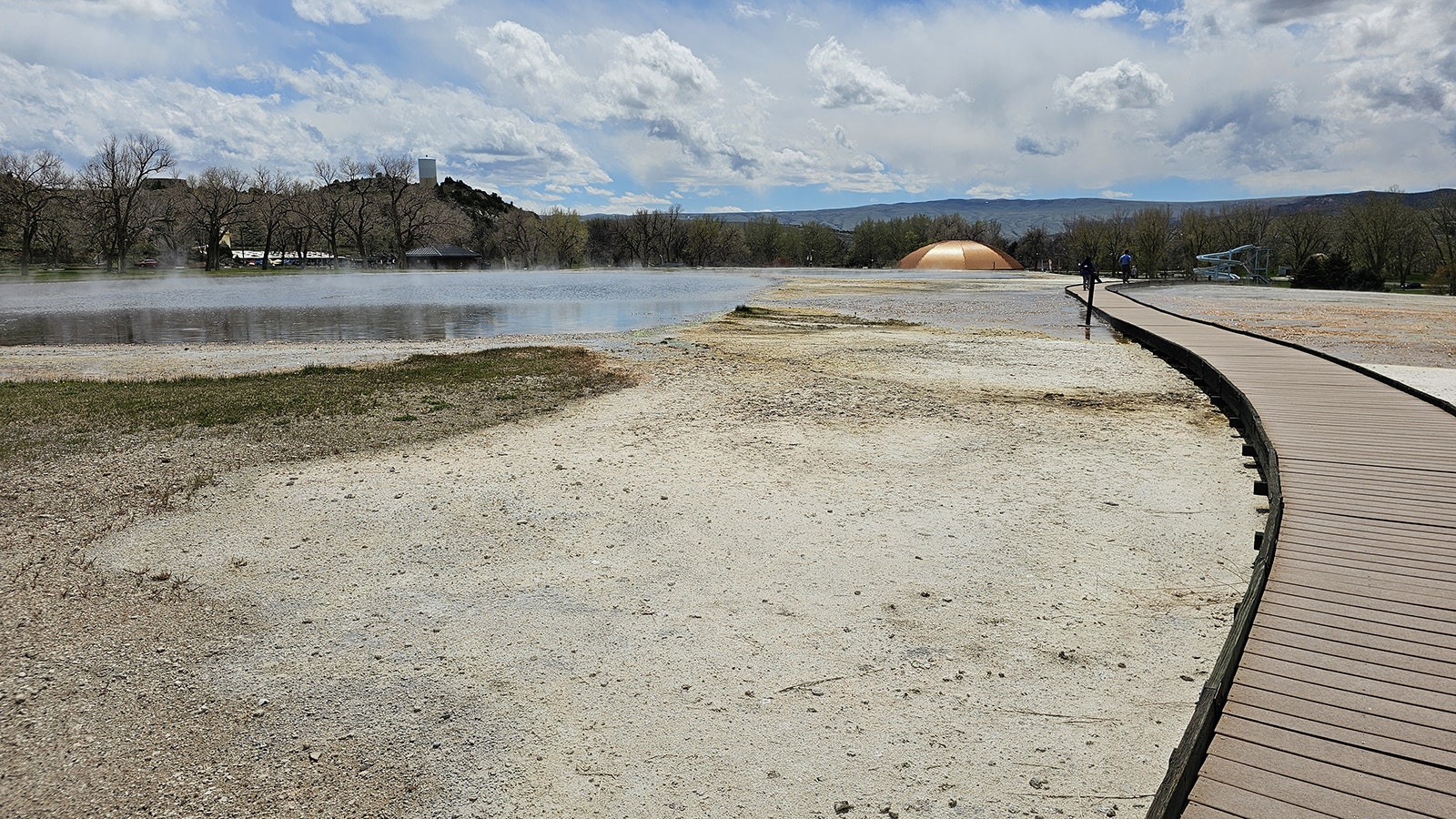 The Teepee Pool's copper dome shines in the distance behind the hot spring at Hot Springs State Park. A boardwalk has been constructed around the spring so that guests can walk around it and explore without damaging any of its fragile features.