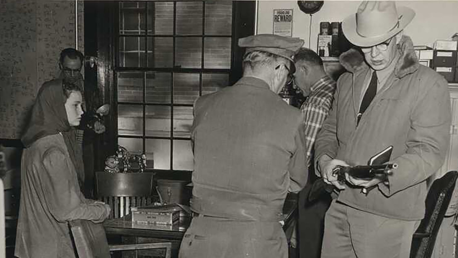 Natrona County Deputy Sheriff Bill Romer, right, examines one of the weapons taken during the Starkweather arrest. Caril Fugate stands behind the chair at left.