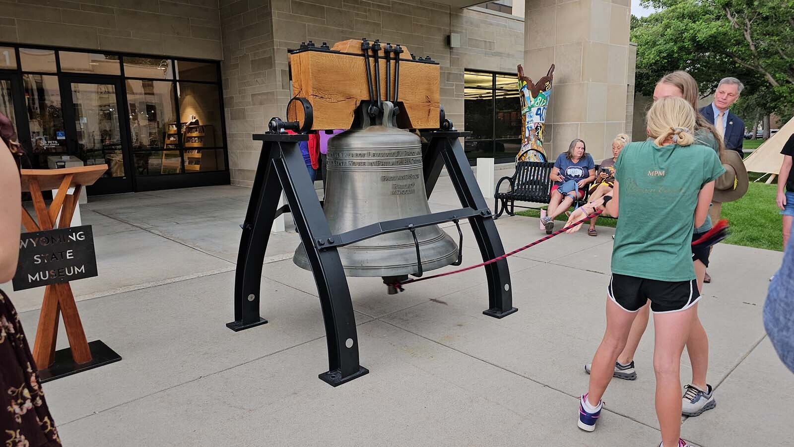 Grace Vetter and Maddie Paulson tug on the red and blue rope attached to the Liberty Bell to give it a loud ring while Gov. Mark Gordon looks on.