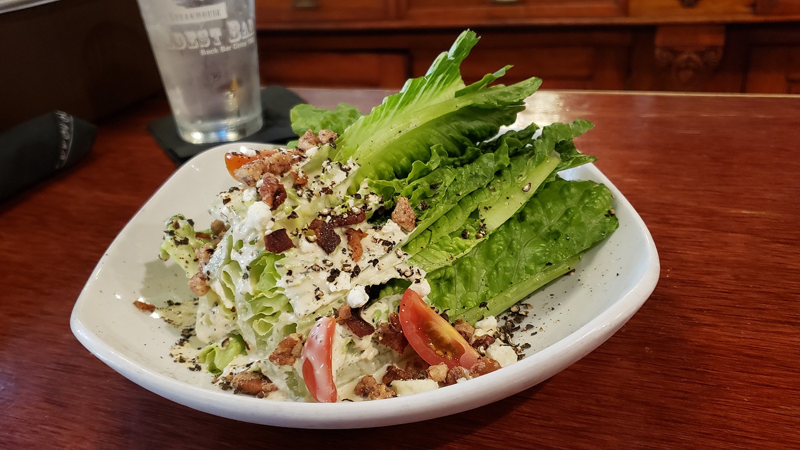 Blue cheese dressing on a romaine wedge salad with fresh tomato, candied bacon and nut crumbles.